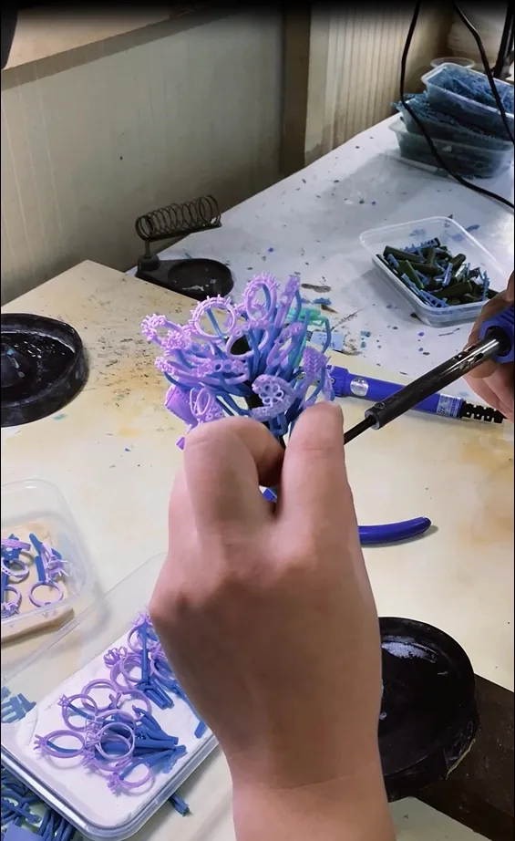 Hands preparing purple jewelry wax models at a workbench